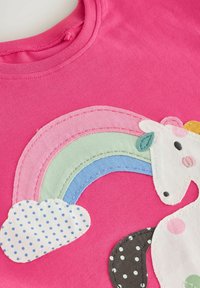 Das rosa Baumwoll-T-Shirt verfügt über ein appliqué Einhorn mit einem mehrfarbigen Regenbogen und einer gepunkteten Wolke, die lebendige Farben und Texturen zur Schau stellen.