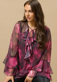 Blusa trasparente con motivo floreale rosa e nero, con rouches sul davanti, colletto a fiocco e maniche svasate. Tessuto liscio e leggero.