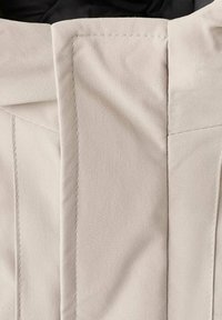 Primer plano de tela beige que muestra las costuras cosidas y una textura suave, con un elemento de diseño doblado y un interior negro en contraste.