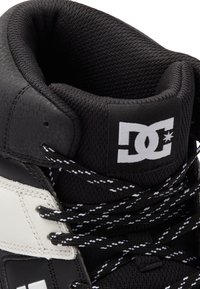 High-top sneaker featuring black leather and mesh materials, white accents, black and white laces, and a prominent DC logo on the tongue.