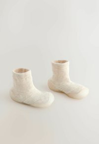 Gestrickte Socken in Cremefarbe und -struktur, kombiniert mit einer glatten, hellen Gummisohle für zusätzlichen Halt und Langlebigkeit.