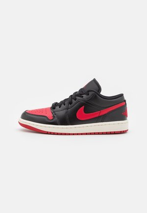 Black and red low-top Nike Air Jordan 1 sneaker with red swoosh logo and white midsole, isolated on white background.