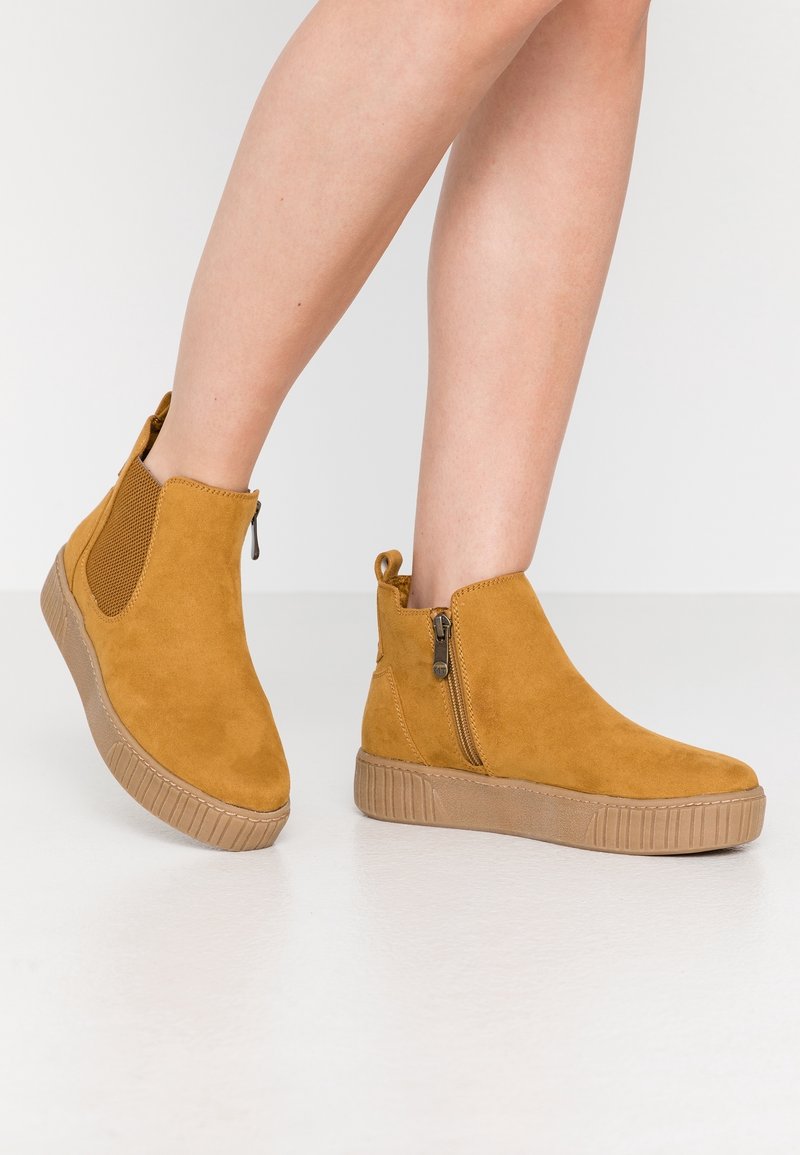 Ankle boots vaale suede se, side zipper, elastic panel aur textured rubber sole ke sath. Square toe aur stitched detailing design ko enhance karti hai.