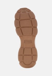 Suola di scarpa in gomma con texture ondulata e a reticolo, di colore beige, dotata di logo "GUESS" in rilievo e un modello di battistrada prominente per una buona trazione.