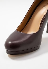 Burgundy leather high heel shoe with a rounded toe, platform sole, and textured finish. Interior lined with beige material.