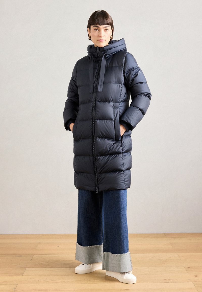 Puff jakke i marineblått med hette, med glidelås foran, quiltet design og to sidelommer. Kombinert med vide denimbukser.
