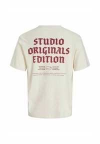 Grietos medvilnės marškinėliai su trumpomis rankovėmis. Drąsus bordo tekstas ant nugaros skelbia "STUDIO ORIGINALS EDITION" kartu su kitais prekiniais ženklais.