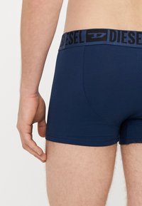 Boxers briefs en coton bleu marine avec une ceinture élastique noire, portant le nom de la marque « DIESEL » en lettres épaisses. Texture lisse et coupe ajustée.