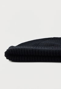 Gorro de malha canelada preto, dobrado plano numa superfície branca, mostrando a textura e o detalhe da borda.