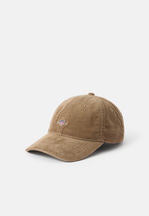 Casquette de baseball en velours côtelé marron clair avec un petit emblème brodé au centre avant, placée sur un fond blanc uni.