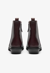 Botas de tobillo de cuero marrón con una textura suave, cremalleras laterales y un tacón negro bajo, diseñadas para un uso seguro y cómodo.