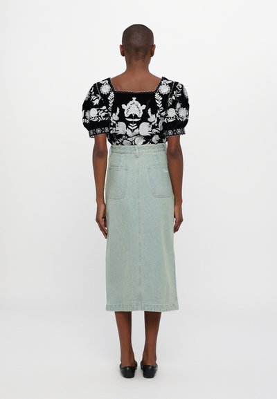 Μαύρη μπλούζα με κεντημένα λουλούδια και φουσκωτά μανίκια, συνδυασμένη με μια ανοιχτόχρωμη τζιν μίντι φούστα που διαθέτει πίσω τσέπες και λεπτομέρεια στη μέση με ζώνη.