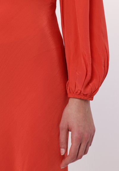 Rode jurk met lange, opbollende mouwen. De stof heeft een gladde textuur met een zichtbare glans. De manchetten zijn met elastiek aangetrokken voor een nauwsluitende look.