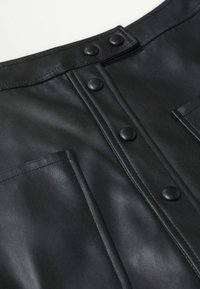 Gros plan sur un vêtement en cuir noir avec des boutons-pression noirs mats et des détails de couture visibles.