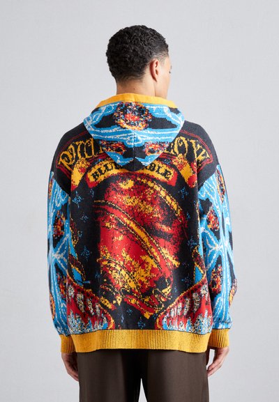 Colorful knitted hoodie with blue, red, and black patterns. Features a yellow ribbed hem and hood with graphic details on the back.