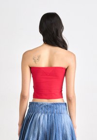 Rdeča brezramna kratka majica iz raztegljivega materiala, v kombinaciji z modrim plisiranim jeans krilom. Ima prilegajočo zasnovo in čisto površino.