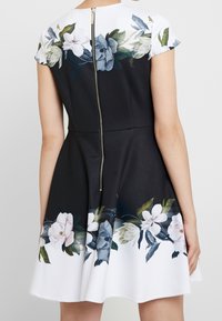 Robe noire avec un motif floral sur l'ourlet et les épaules, dotée de manches courtes et d'une fermeture éclair en métal visible au dos.