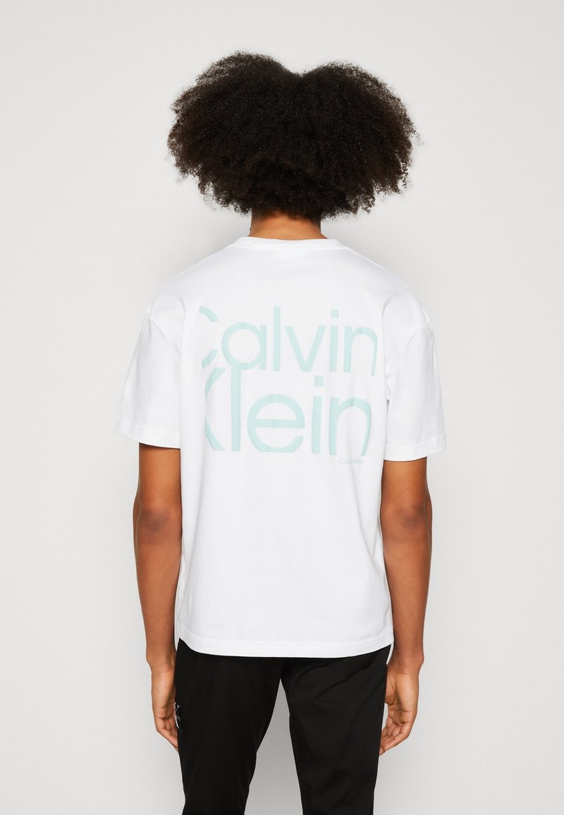 Bílá bavlněná tričko s velkým mátově zeleným logem "Calvin Klein" potištěným na zadní straně. Design s kulatým výstřihem a krátkými rukávy.