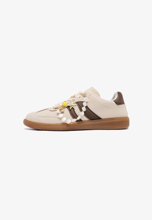 Baskets beiges avec des rayures marron, semelle en gomme, et un bracelet décoratif avec un coquillage et une étoile de mer drapé sur les lacets sur fond blanc.