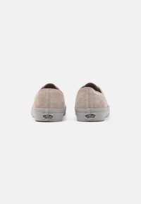 Une paire de baskets Vans en suède beige vue de l'arrière, montrant des semelles en caoutchouc grises avec le logo "Off The Wall" sur un fond blanc.