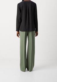 Blusa nera a maniche lunghe con scollatura rotonda, abbinata a pantaloni verdi a vita alta e gamba larga, caratterizzati da una texture liscia e una vestibilità sartoriale.