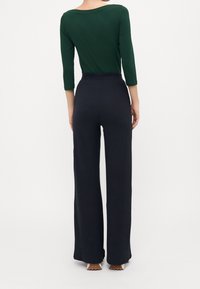 Groene, getailleerde top met lange mouwen gecombineerd met hoge taille, ribbelachtige marineblauwe wijdlopende broek, met een gladde textuur en subtiele horizontale lijnen.