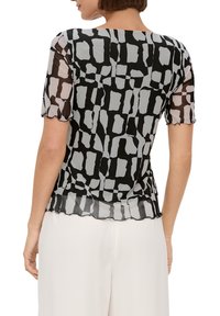 Zwarte sheer top met een geometrisch grijs patroon, korte mouwen en een geschulpte zoom. Lichtgewicht stof voegt textuur en visuele interesse toe.