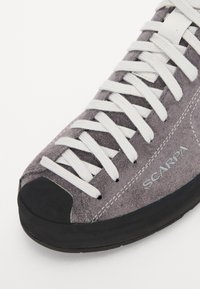 Graue Wildleder-Kletterschuhe mit weißen Schnürsenkeln, Gummikappe und schwarzer Sohle. Verfügt über ein Logo und Nähdetails an der Seite.