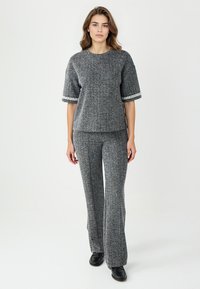 Grijs, getextureerd outfit met korte mouwen en wijde broekspijpen. Geaccentueerd met een lichte bies aan de mouwen. Zwarte schoenen maken de look compleet.