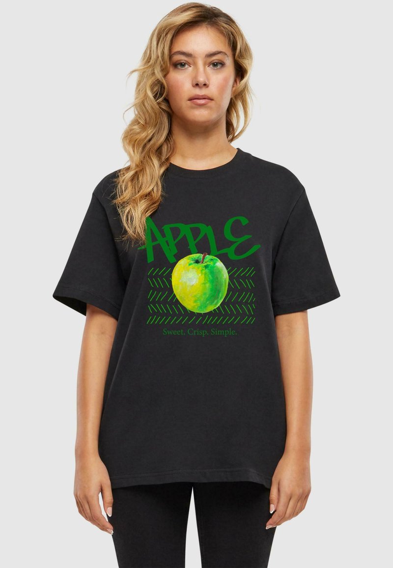 Sort bomulds T-shirt med et grafisk billede af et grønt æble og ordet "APPLE" i grøn, med et tekstureret mønster og slogan nedenfor.