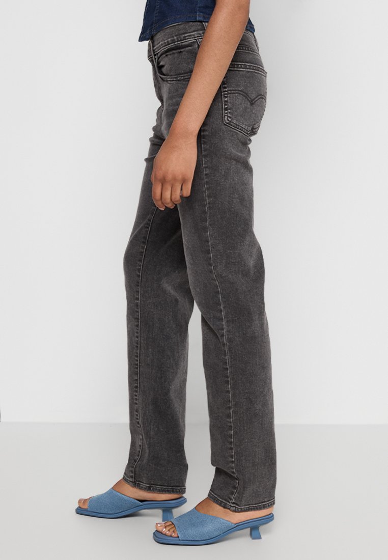 Jeans de denim negros de pierna recta con un acabado desgastado, combinados con sandalias de punta abierta azules que tienen un tacón bajo cuadrado.