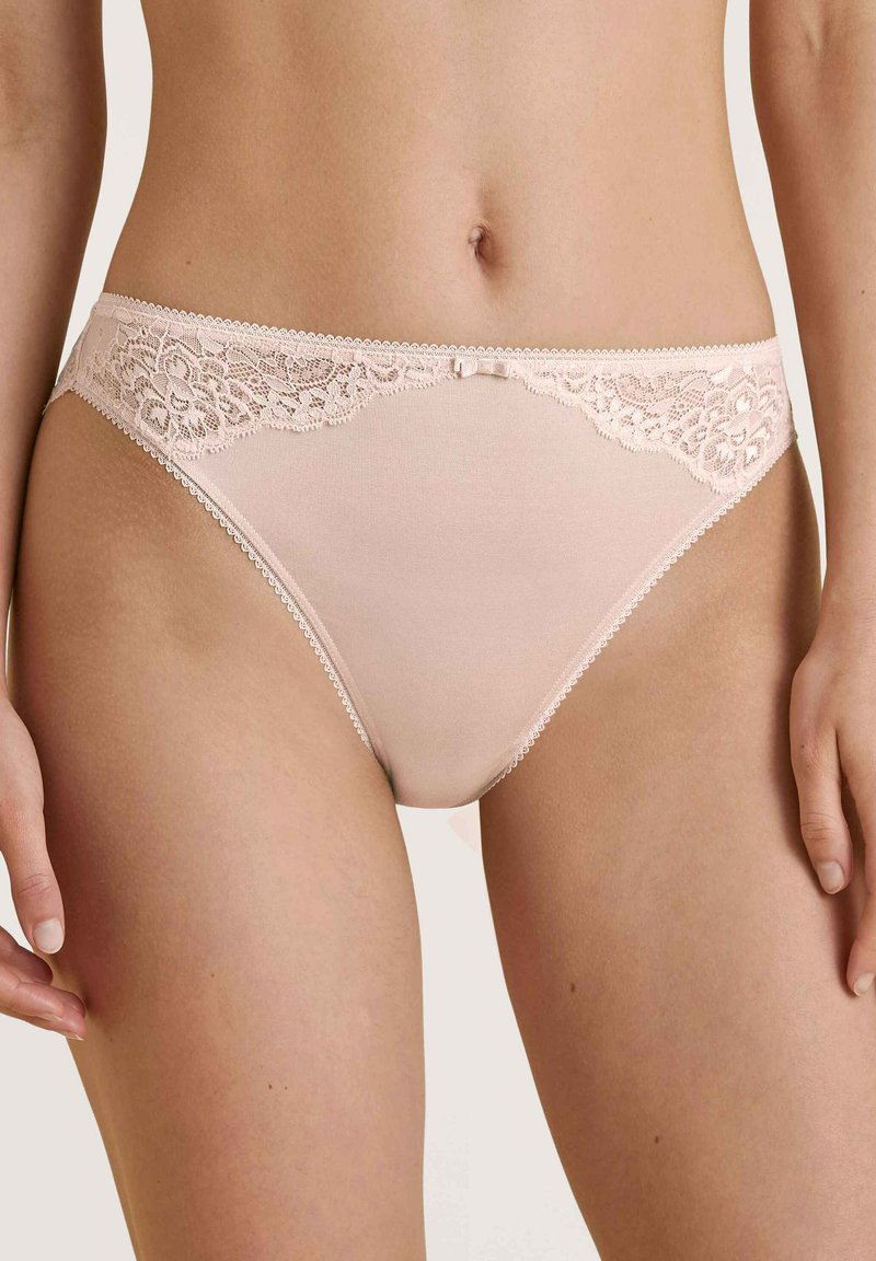 Lichtroze panties met kant langs de tailleband, een kleine strikaccent in het midden en geschulpte randen langs de beenopeningen.