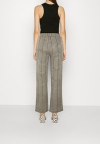 Gray plaid trousers with a relaxed fit, featuring a high waistband and wide legs. Paired with black block-heeled shoes with a checkered pattern.