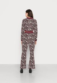 Conjunto de dois peças com estampa de zebra em bordô e creme, apresentando um tecido texturizado, mangas longas e calças flare com uma cintura ajustada.