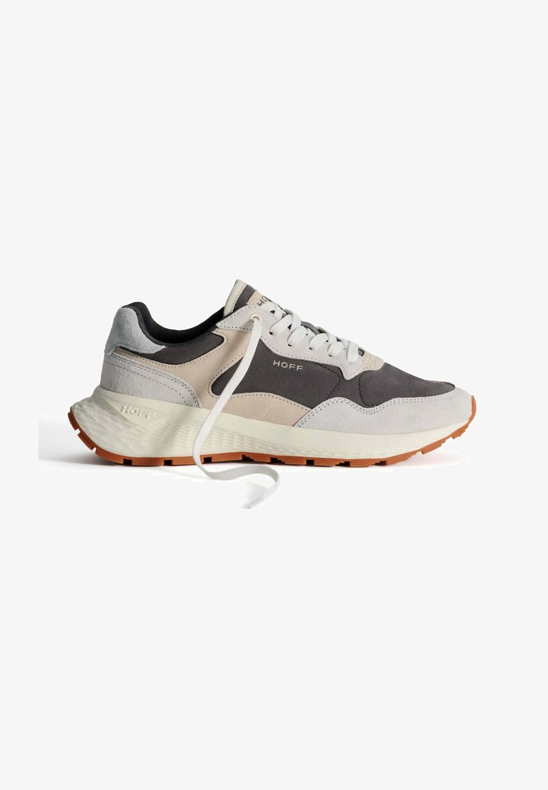 Zapatilla de running ligera con una parte superior de gamuza gris y beige, acentos negros, cordones blancos y una entresuela blanca texturizada con una suela naranja.