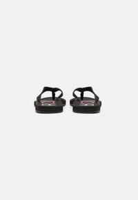 Tongs noires avec une sangle texturée et un semelle ergonomique. La semelle présente un détail de logo rose. Design simple et plat adapté à un usage décontracté.