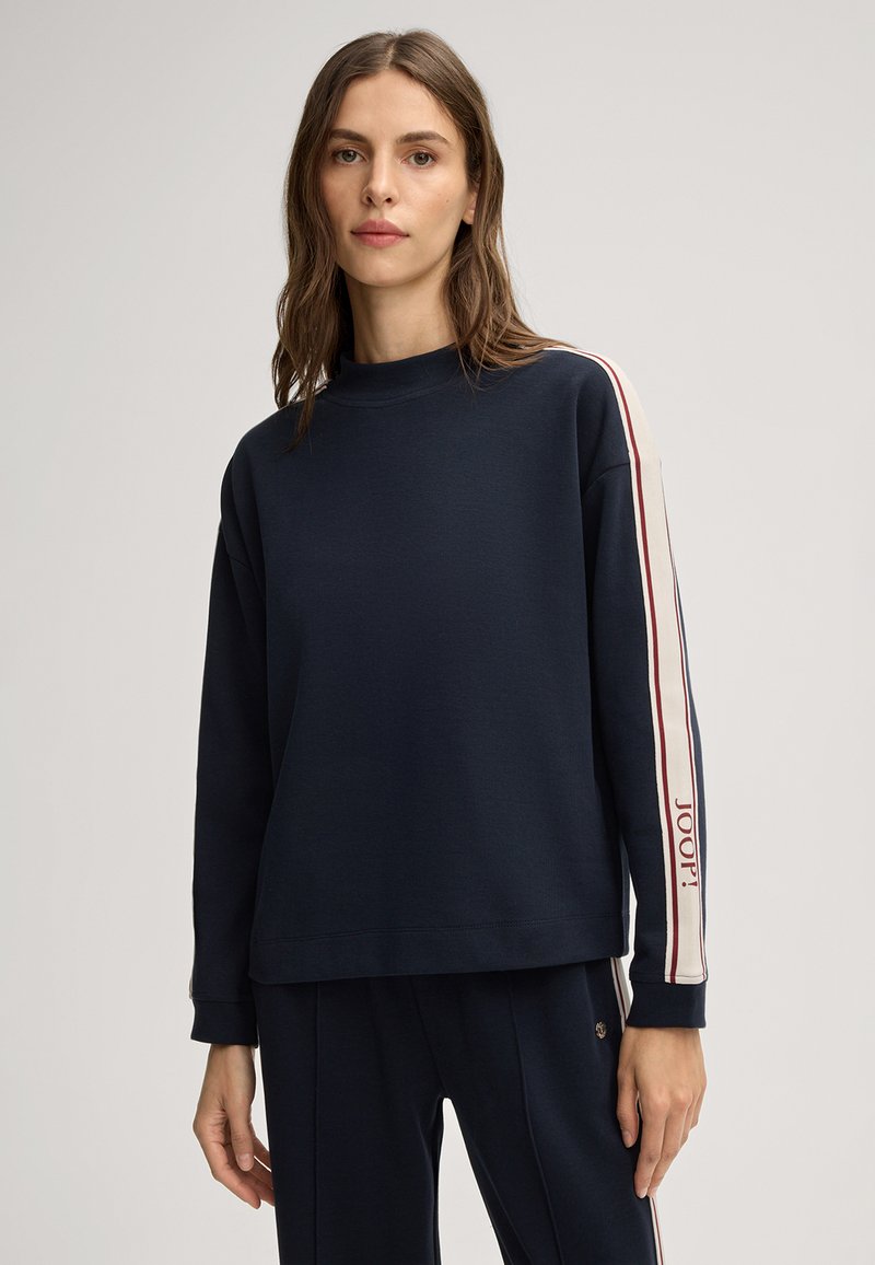 Navy sweatshirt met hoge hals, lange mouwen en witte en rode strepen langs de armen, met het "JOOP!" logo op de linker mouw.