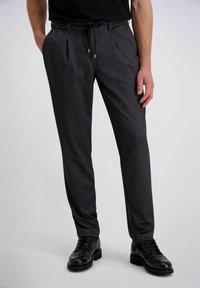 Zwarte patroonbroek met een trekkoord in de taille, gemaakt van een gestructureerde stof en met plooien. Gecombineerd met zwarte veterschoenen.