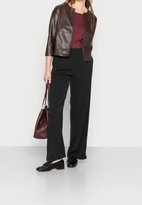 Hnědá kožená bunda, maroon top, černé široké kalhoty, černé boty. Drží burgundskou kabelku. Jednoduchý, moderní design. Hladká textura.