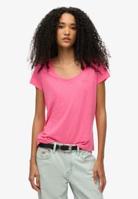 Camiseta rosa de manga corta con escote en forma de u, hecha de un tejido ligero. Combinada con jeans de mezclilla claros y un cinturón negro.