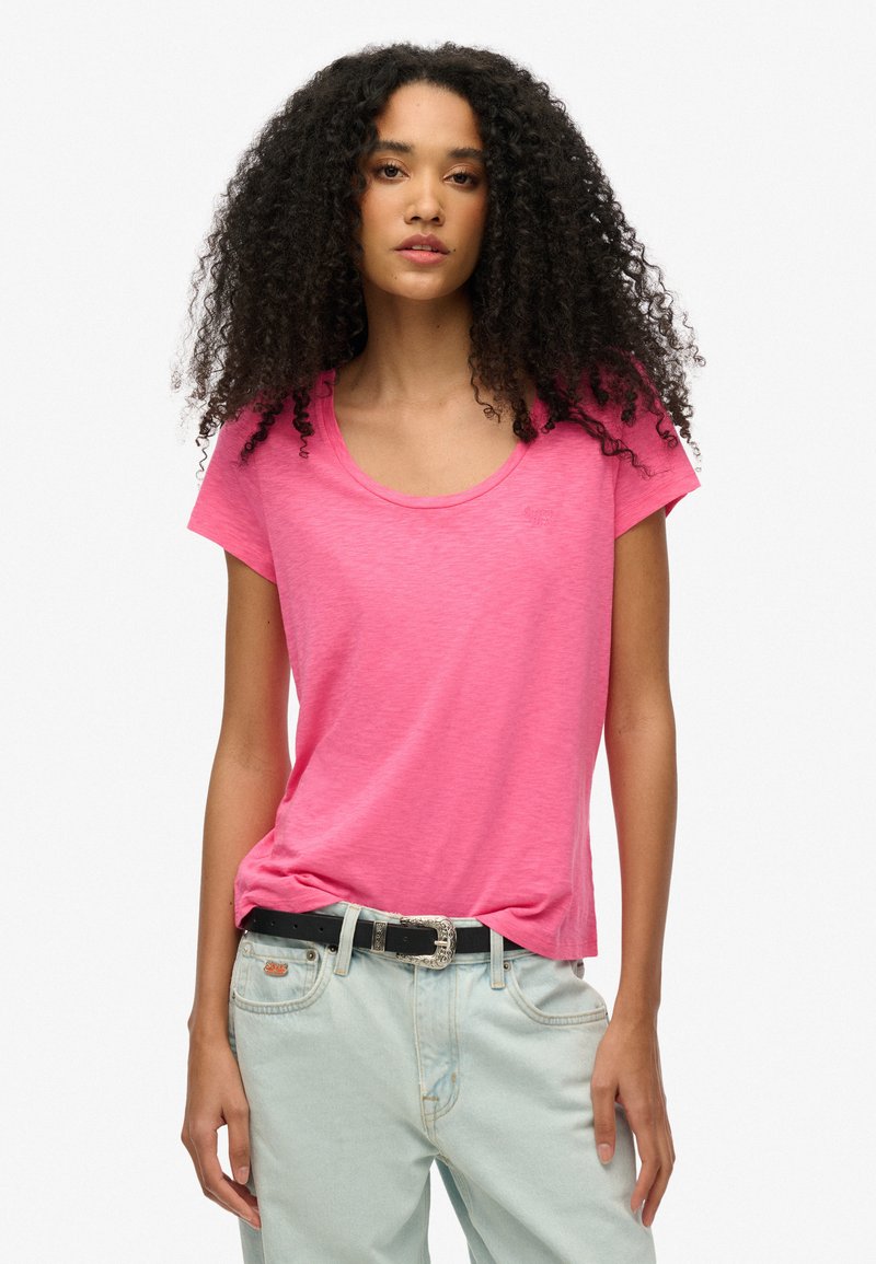 Camiseta rosa de manga corta con escote en forma de u, hecha de un tejido ligero. Combinada con jeans de mezclilla claros y un cinturón negro.