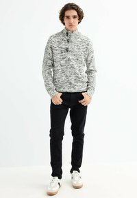 Suéter de punto moteado en gris y blanco con cuello alto y tres botones, combinado con pantalones ajustados negros y zapatillas blancas.