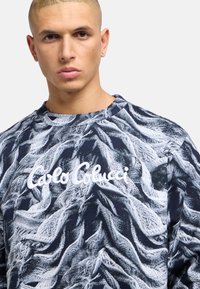 Navy blue sweatshirt with textured white wave pattern and embroidered brand name "Carlo Colucci" in white on the front.