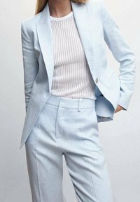 Costume bleu clair sur mesure avec une veste slim et un pantalon assorti, associé à un haut côtelé crème texturé. Finition en tissu lisse.