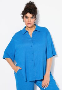 Camicetta blu a maniche corte con colletto, tessuto testurizzato e vestibilità comoda, abbinata a pantaloni blu coordinati.