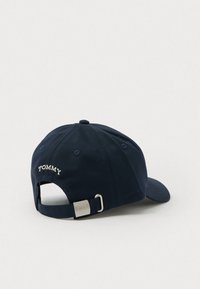 Tengerészkék baseball sapka, pamutból készült, ívelt karimával, hátul állítható pánttal, és fehér színű "TOMMY" hímzéssel a hátán.