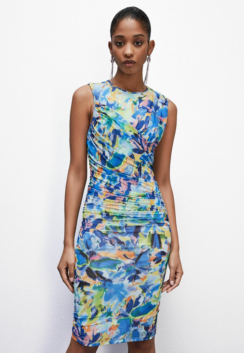 Dopasowana, bezrękawnikowa sukienka w intensywnym niebieskim kolorze z abstrakcyjnymi, wielokolorowymi wzorami. Posiada marszczenia po bokach, które dodają tekstury.