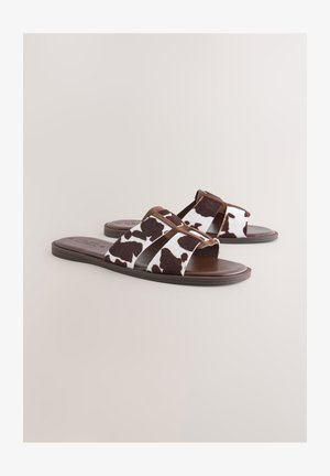 Sandales slide à imprimé vache avec des accents marron, comprenant deux larges bandes, une semelle lisse et une texture douce.