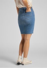 Jupe crayon en denim bleu clair, avec une silhouette ajustée, une longueur mi-cuisse et des poches arrière. Associée à des baskets montantes beiges.