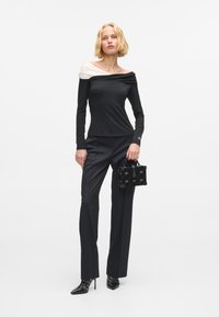 Czarny top z długim rękawem z białymi opadającymi ramionami, w połączeniu z czarnymi dopasowanymi spodniami i małą czarną torebką w wzór. Czarne szpilki.